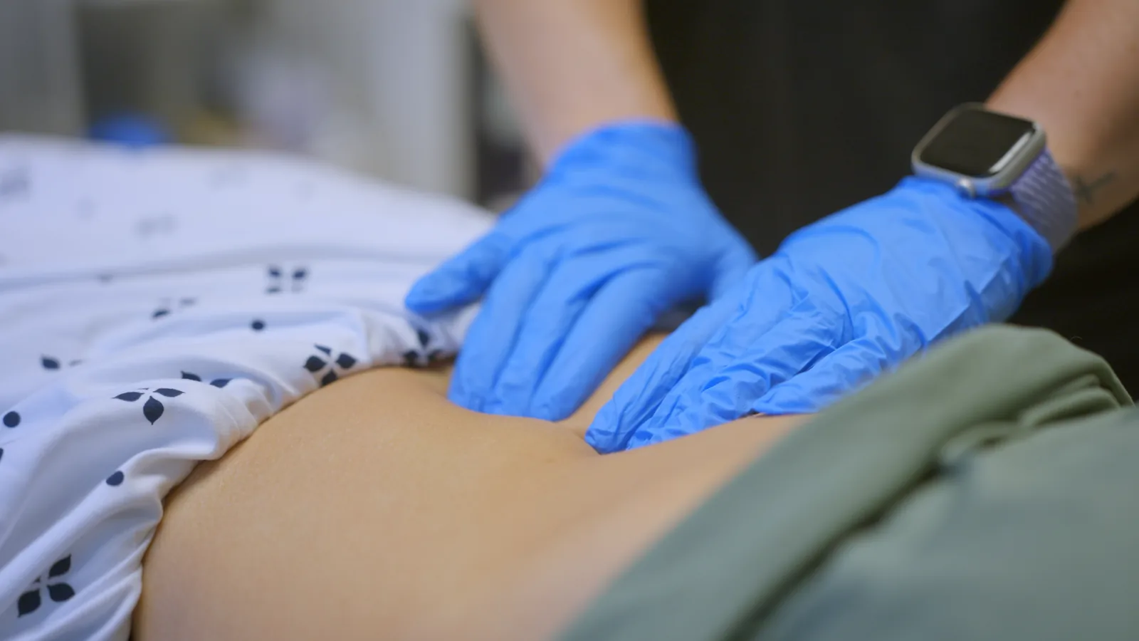 A pelvic health physical therapist's gloved hands assessing a patient's abdomen
