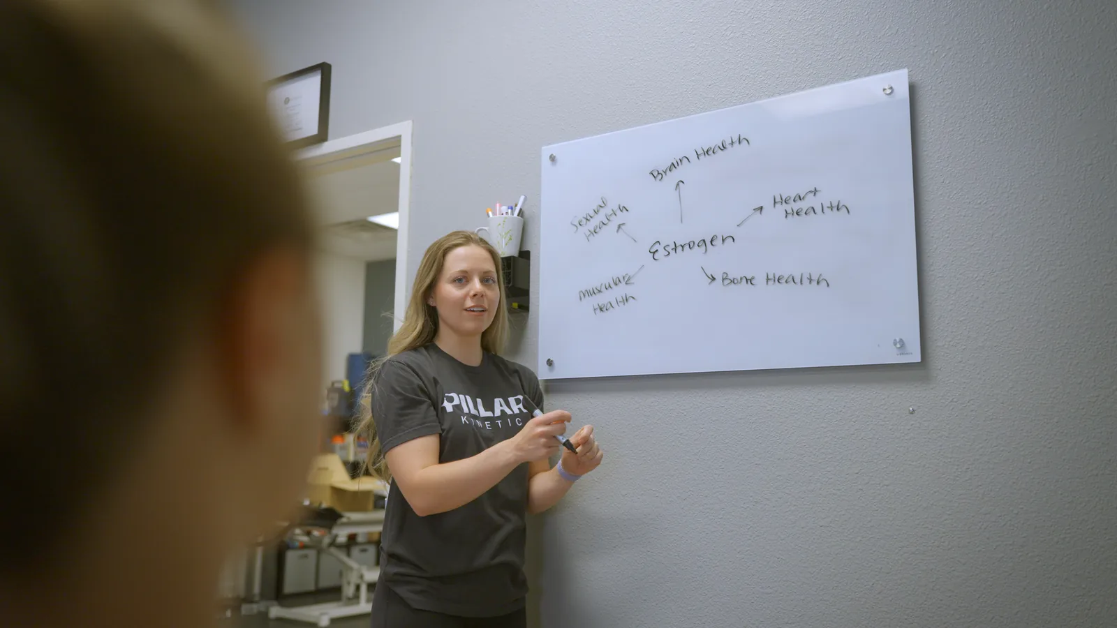 A physical therapist explaining on a whiteboard how estrogen affects the body