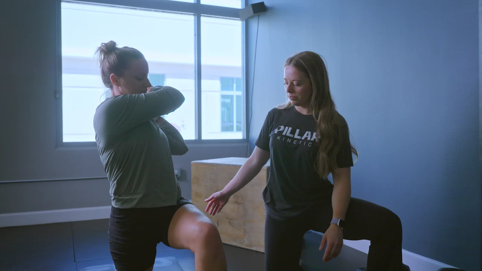 A physical therapist coaching a woman through a lunge in the clinic gym