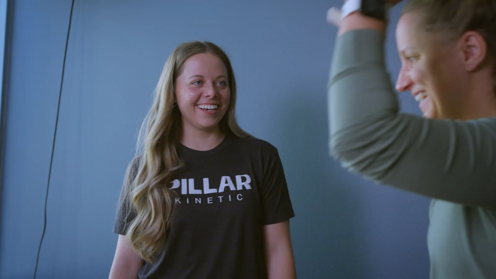A patient raising one arm overhead as her physical therapist laughs beside her