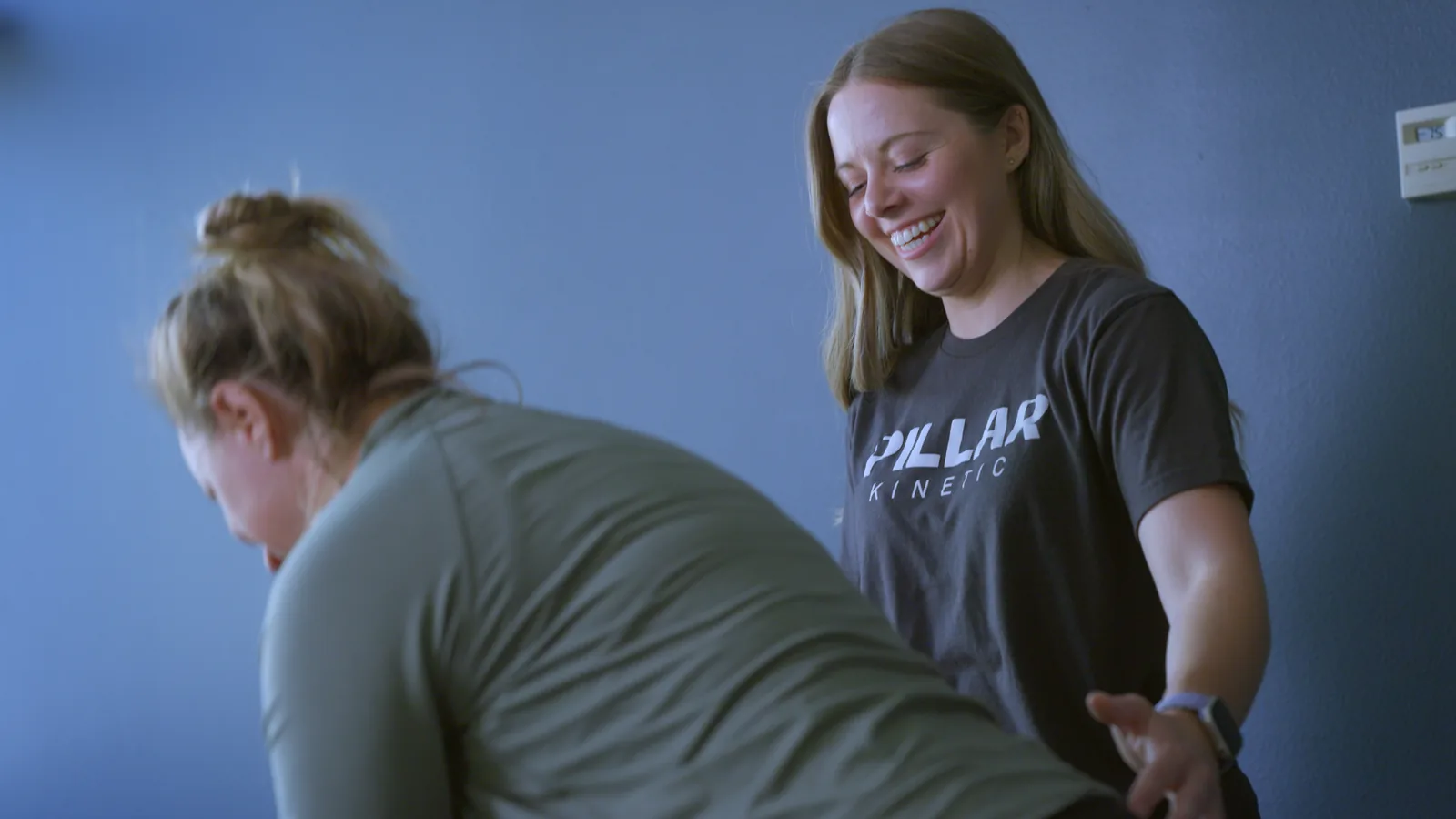 A physical therapist smiling as she guides a woman's hips through a movement