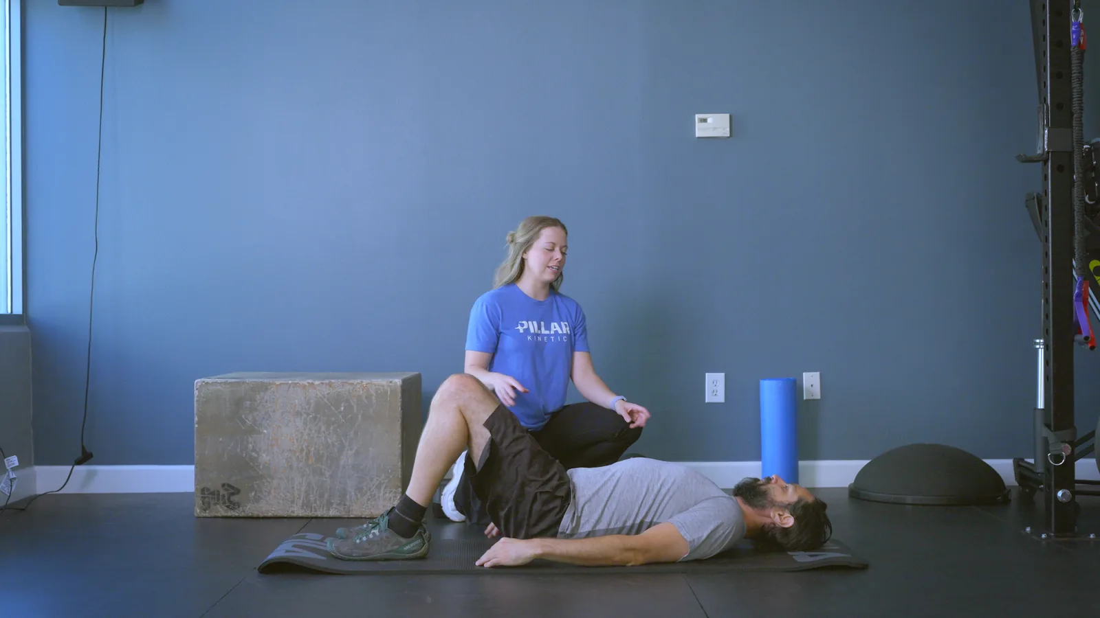 A physical therapist kneeling beside a man lying on a mat with his knee bent