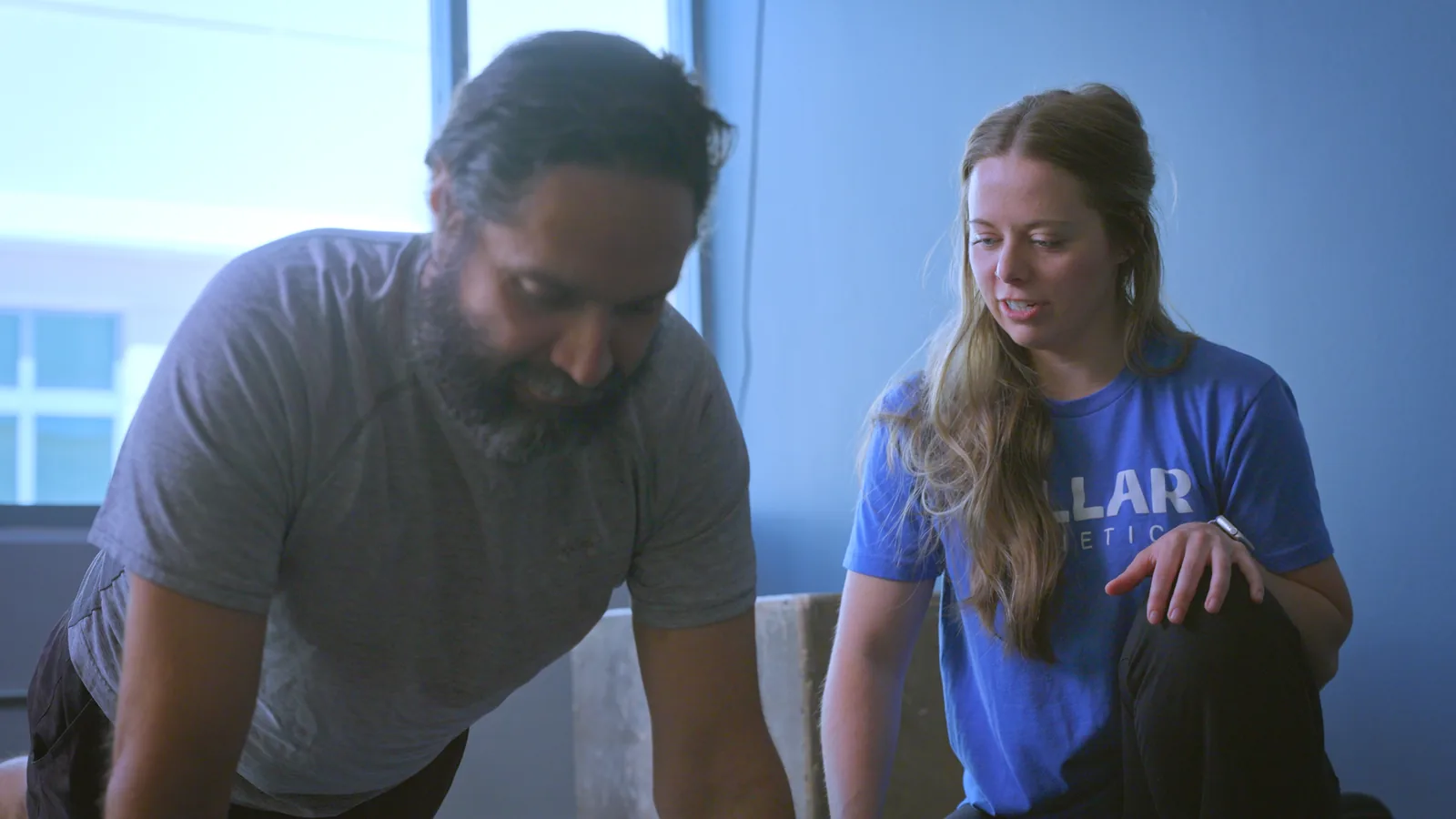 A physical therapist watching a patient's movement up close in the clinic gym