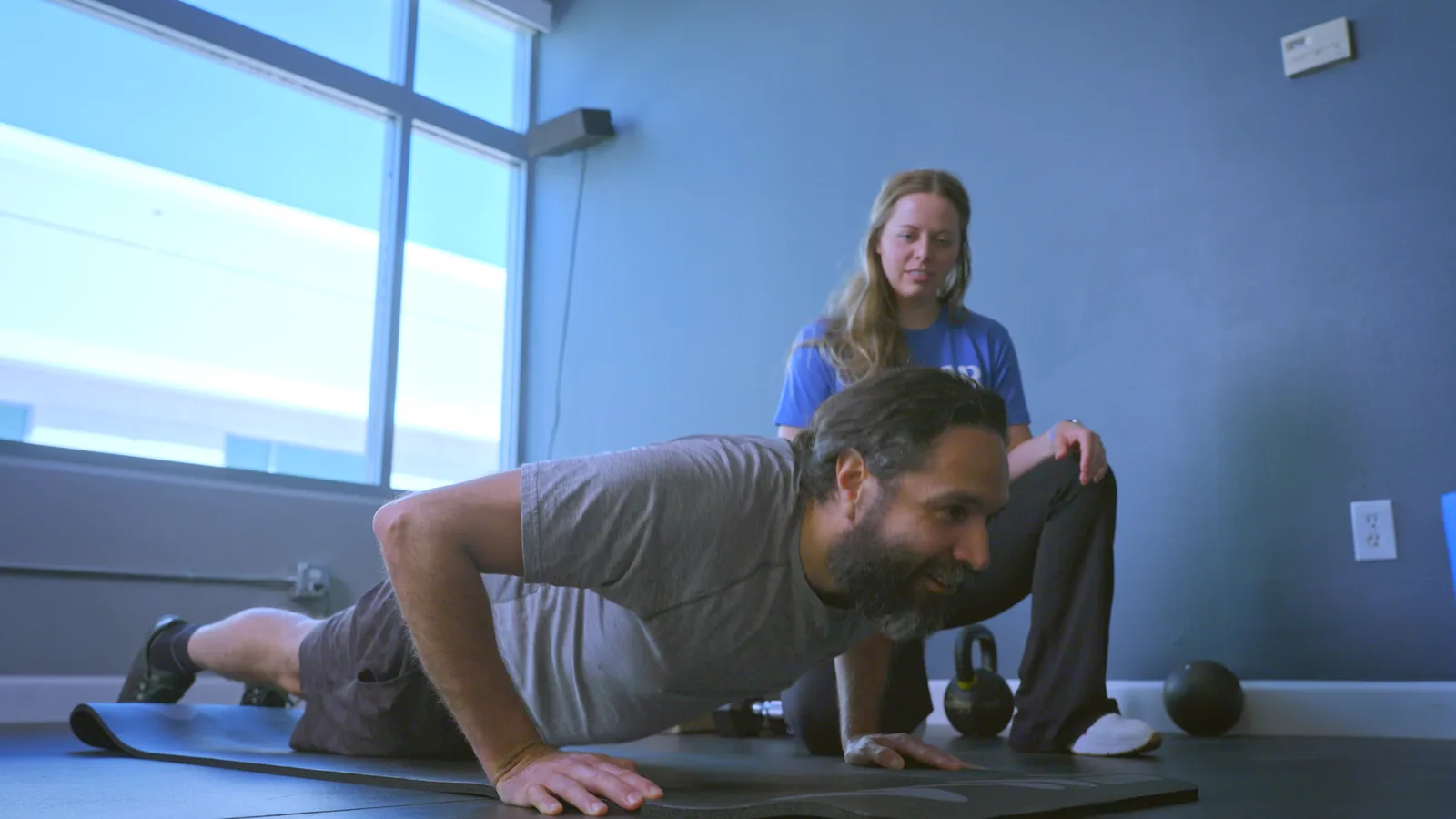 A man holding a push-up while a physical therapist kneels behind him, watching his position