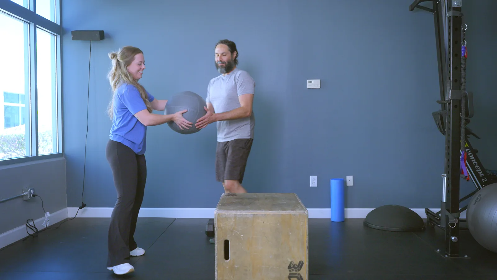 A physical therapist passing a medicine ball to a patient beside a plyometric box