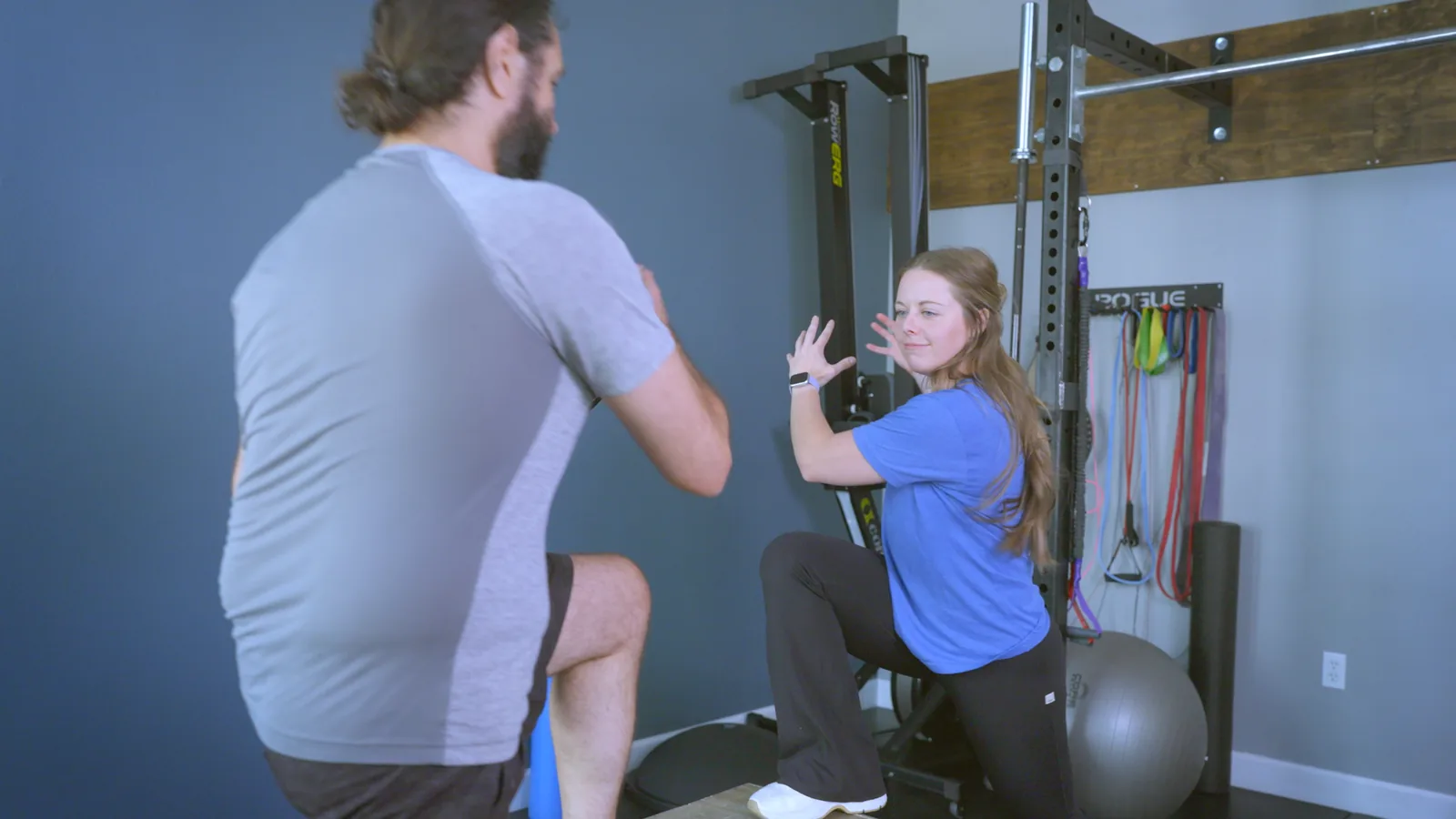A physical therapist demonstrating a split squat as a man copies her in the clinic gym