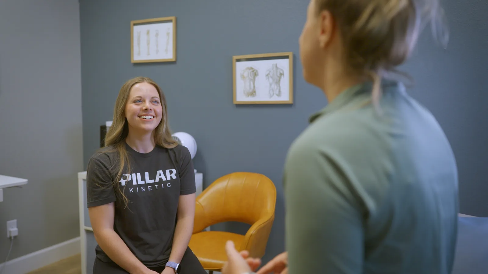 A Pillar Kinetic physical therapist smiling as she talks with a patient in a treatment room