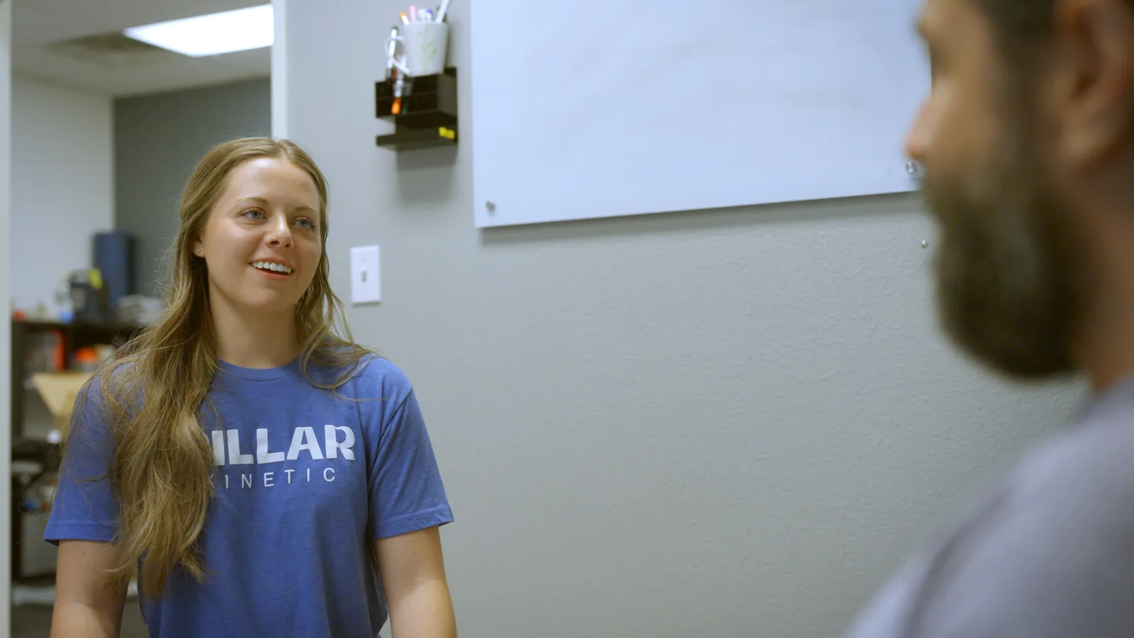 A Pillar Kinetic physical therapist in a blue clinic shirt smiling as she talks with a patient