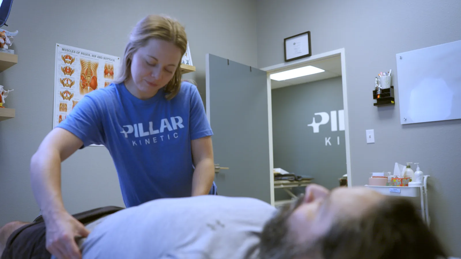 A physical therapist with her hands on a patient's lower back as he lies on the treatment table