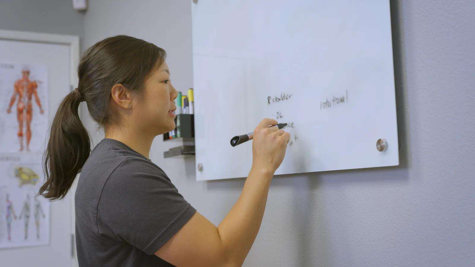 A physical therapist writing on a whiteboard in a treatment room