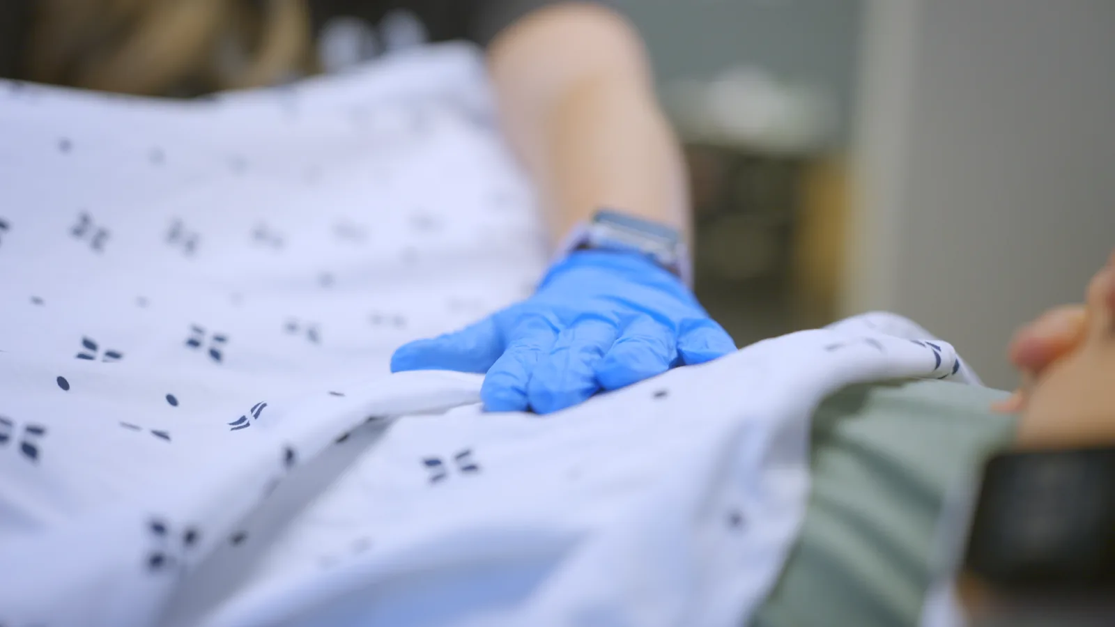 A pelvic health physical therapist's gloved hand on a patient's abdomen over the gown