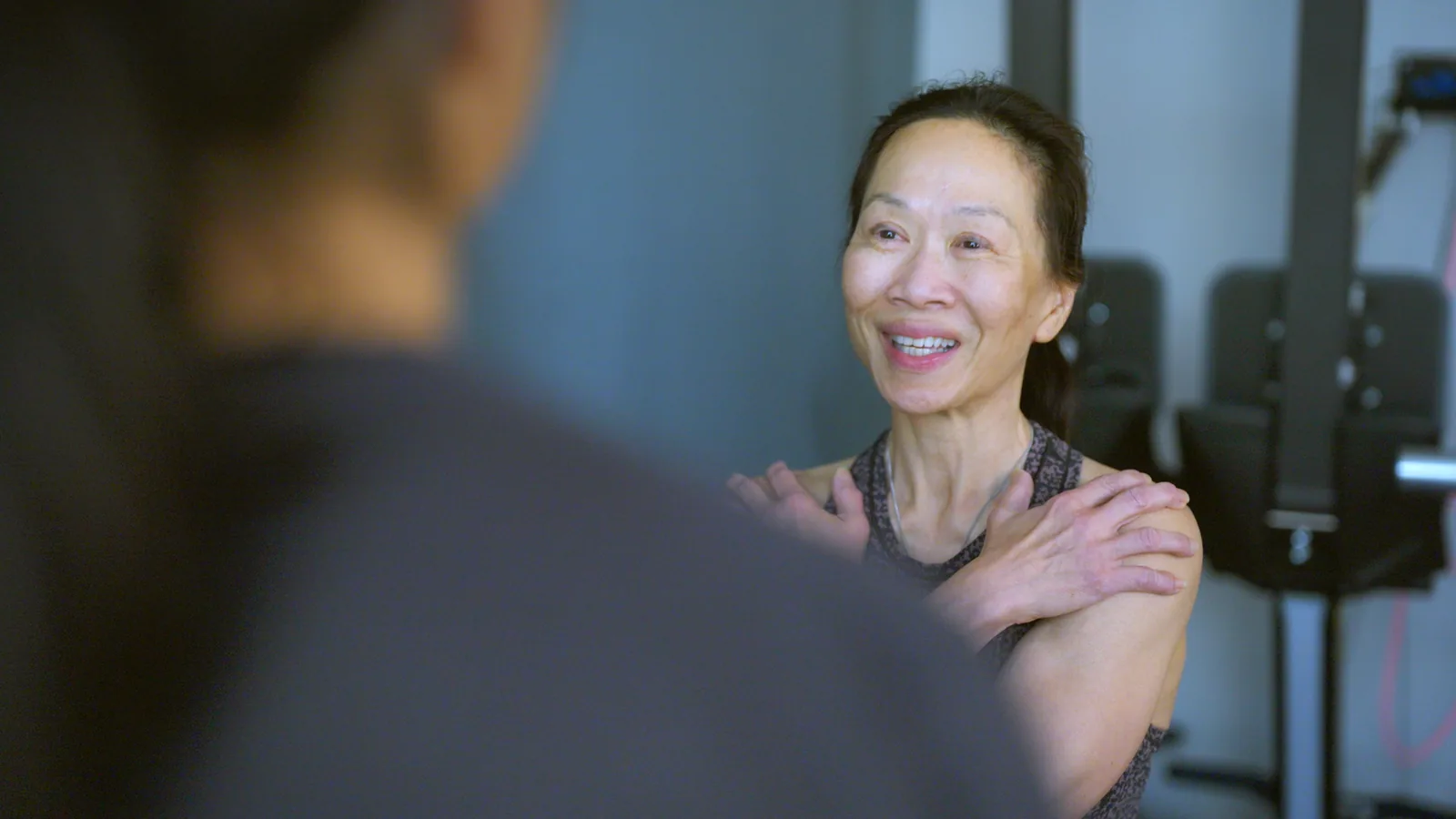 An older patient smiling as she talks with her physical therapist in the clinic gym
